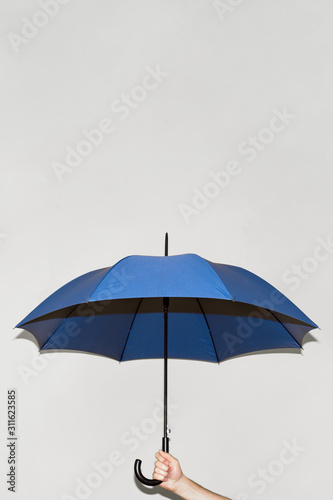 A man holds a blue umbrella in his hand against a gray wall. Open space above the umbrella. Concept autumn  color of the year 2020  business  protection.