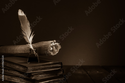 Quill pen and rolled papyrus sheets on a wooden table with old books, sepia effect