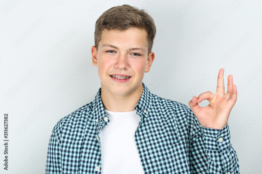 Young man with dental braces showing okay gesture on grey background Young man with dental braces showing okay gesture on grey background