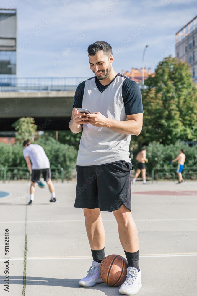 A young sportsman smiles while using his mobile phone in the middle of an urban field