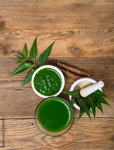 Medicinal Neem leaves in mortar and pestle with neem paste, juice and twigs on wooden background