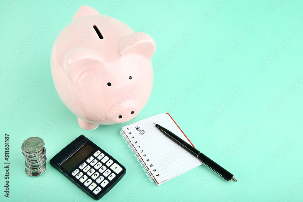 Pink Piggy Bank With Coins Calculator And Notepad On Mint Background pink-piggy-bank-with-coins-calculator-and-notepad-on-mint-background