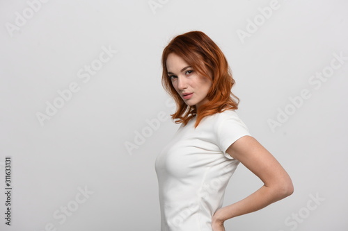 Beautiful redhead girl in a beige dress posing in front of the camera. Portrait on a neutral light background, space for text