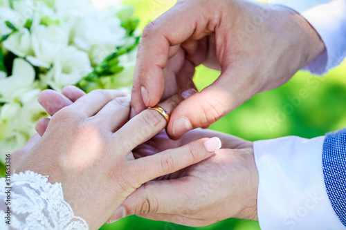 newlyweds exchange rings on the background of a white wedding bouquet