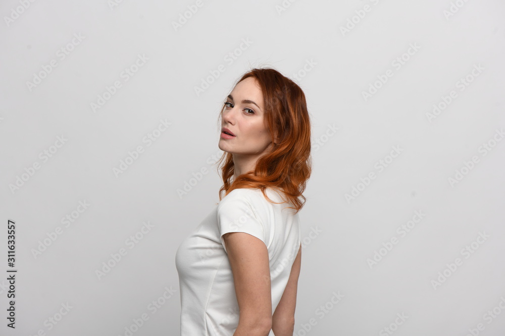 Beautiful redhead girl in a beige dress posing in front of the camera. Portrait on a neutral light background, space for text Beautiful redhead girl in a beige dress posing in front of the camera. Portrait on a neutral light background, space for text