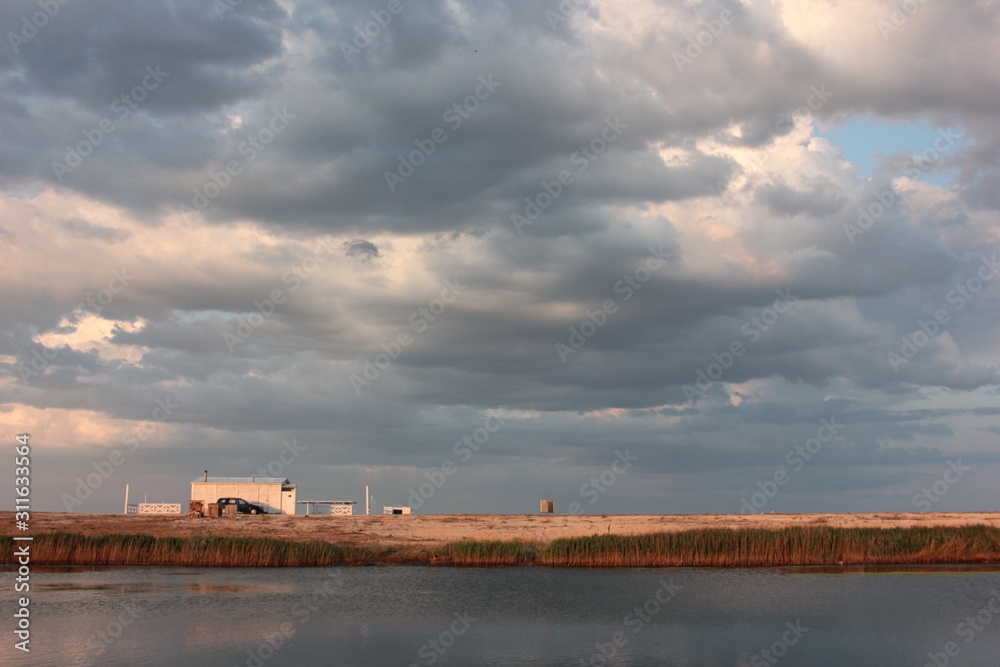 Summer landscape with threatening dramatic sky, sea, lake and white house on the horizon