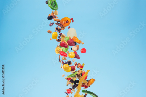 Dried and candied fruits and nuts flying on blue background. Stock photo of healty and nutrient food.