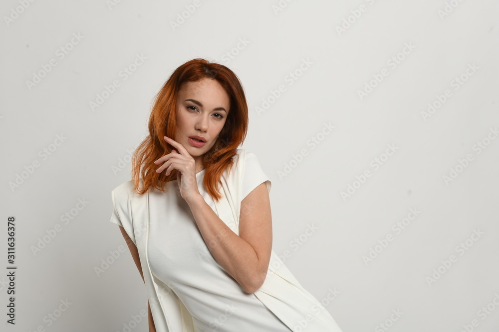 Beautiful redhead girl in a beige dress posing in front of the camera. Portrait on a neutral light background, space for text. Beautiful redhead girl in a beige dress posing in front of the camera. Portrait on a neutral light background, space for text.