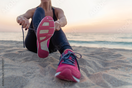 Beautiful slim girl athlete knots sneakers at dawn on the seashore