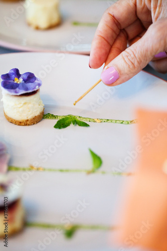 Hand decorating a cheese cake cupcake with a purple flower on top