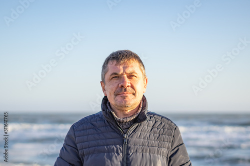Tired man 50 years old on the seashore in casual clothes on a sunny winter day.