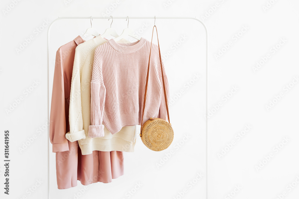 Feminine  warm sweaters and pale pink dress with bamboo bag on hanger on white background. Elegant   fashion outfit. Spring wardrobe. Minimal concept. - obrazy, fototapety, plakaty 