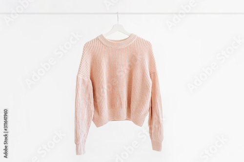 Feminine pale pink warm sweater on hanger on white background. Elegant  jumper  fashion outfit. Spring wardrobe. Minimal concept.