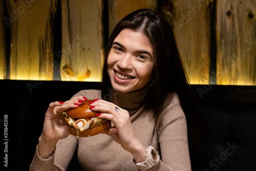 Close up portrait of a smiling hungry young woman eating burger