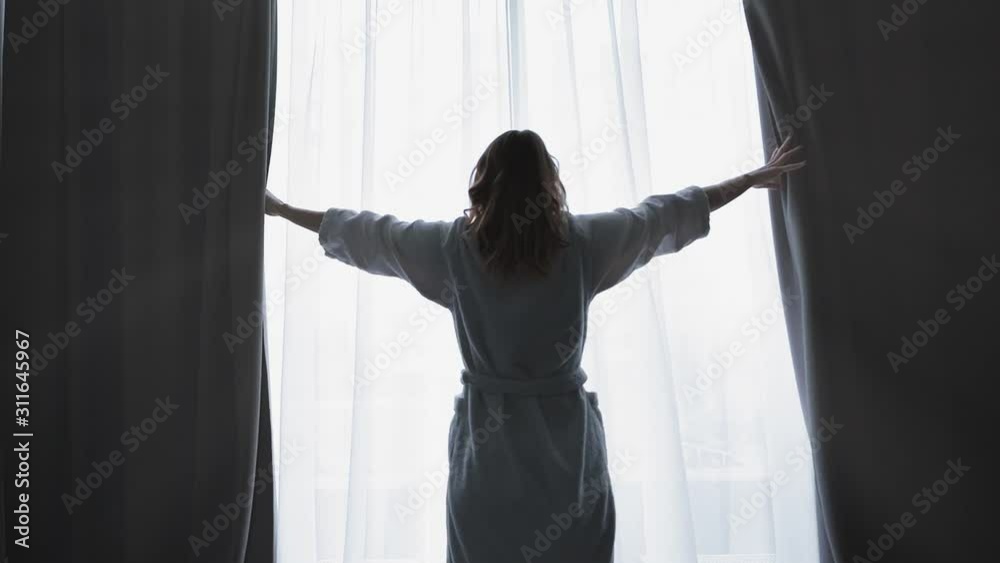 Young woman wake up and open the curtains in the morning enjoying sunlight. Slow motion. Feeling happy 