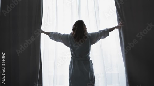 Young woman wake up and open the curtains in the morning enjoying sunlight. Slow motion. Feeling happy  photo