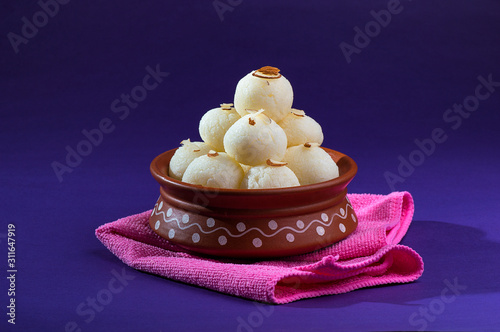 Indian Sweet or Dessert - Rasgulla, Famous Bengali sweet in clay bowl with blue napkin on violet background