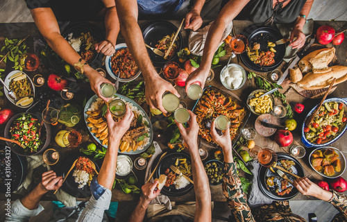 Flat-lay of family clinking glasses over table with Turkish cuisine lamb chops, quince, bean, vegetable salad, babaganush, rice pilav, pumpkin dessert and lemonade, top view. Middle East cuisine