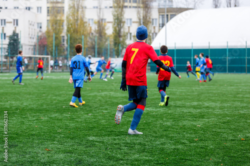 Boys in red and blue sportswear plays football on field, dribbles ball. Young soccer players with ball on green grass. Training, football, active lifestyle for kids concept © Natali
