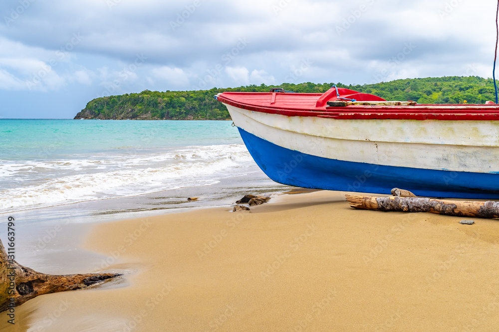 Colorful old wooden fishing boat docked by water on a beautiful beach coast land. White sand sea shore landscape on tropical Caribbean island. Holiday weekend/ summer vacation setting in Jamaica.