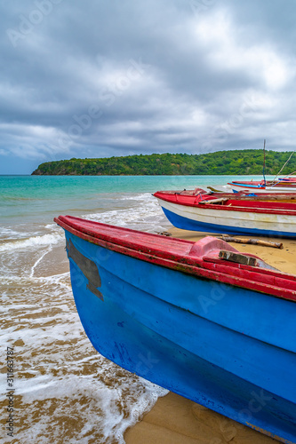 Colorful old wooden fishing boats docked by water on a beautiful beach coast land. White sand sea shore landscape on tropical Caribbean island. Holiday weekend/ summer vacation setting in Jamaica.