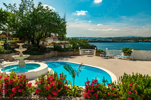 Fototapeta Naklejka Na Ścianę i Meble -  Tropical flower garden with pool and fountain on a mediterranean style oceanfront terrace with mountain view
