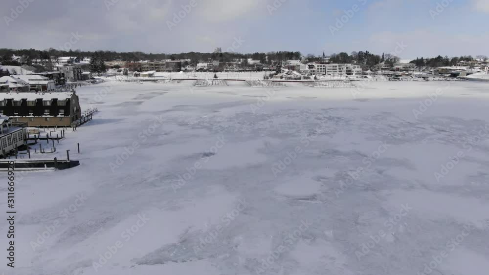 Winter in Northern Michigan in Charlevoix Lake Michigan and the Pine River meet downtown 4K drone shots over forest and open woods in winter snow covered scene round lake frozen no boats Winter in Northern Michigan in Charlevoix Lake Michigan and the Pine River meet downtown 4K drone shots over forest and open woods in winter snow covered scene round lake frozen no boats