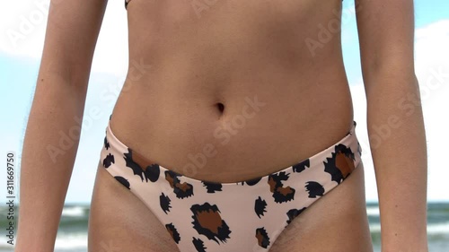 Close-up of a slim belly of a young healthy woman in bikini at the ocean beach.