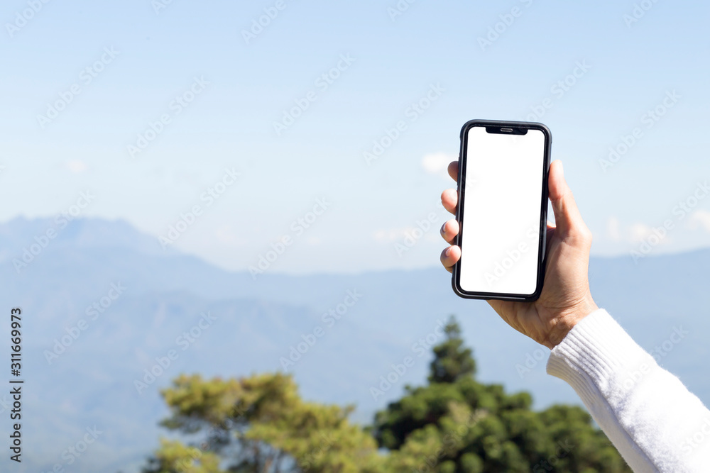 Hand holding smartphone with white screen to add text and sky and mountain background 
