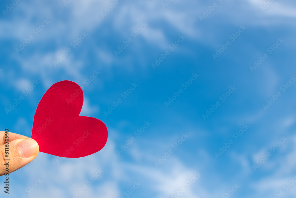 Fototapeta premium Hand’s people show red heart paper and blue sky with clouds. Concept for valentine 's day theme ,Holiday ,Postcard ,Romantic card ,Day off ,Wedding marriage love card.