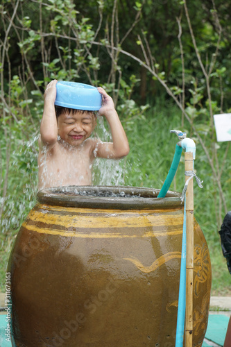 One young Asian kid is taking a bath with fun next to the big clay jar. The little boy is enjoy playing the water at the outdoor park/garden. Urban style showering concept in Asian. photo