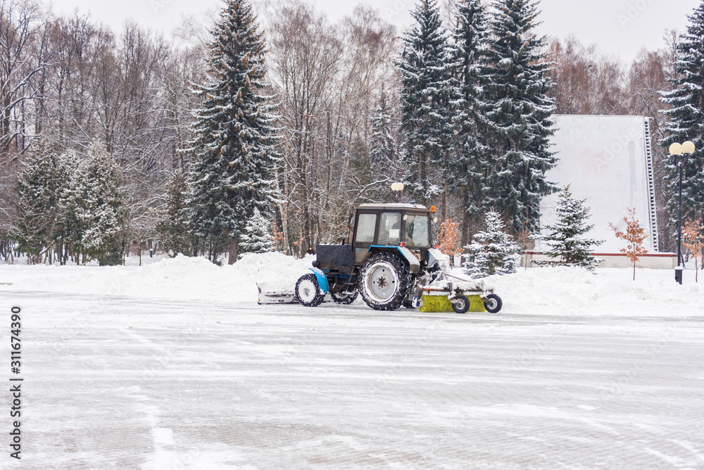 Tractor cleans the snow in the city park Tractor cleans the snow in the city park