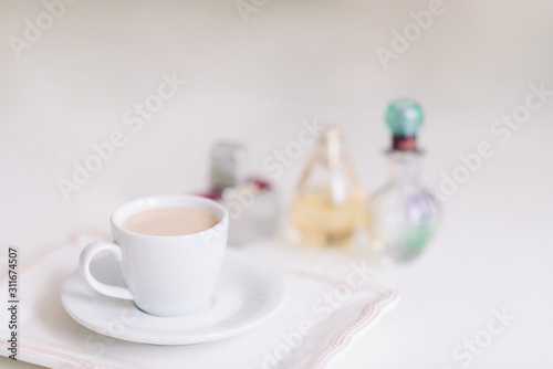 White cup with coffee on a porcelain plate in the background of perfume bottles.