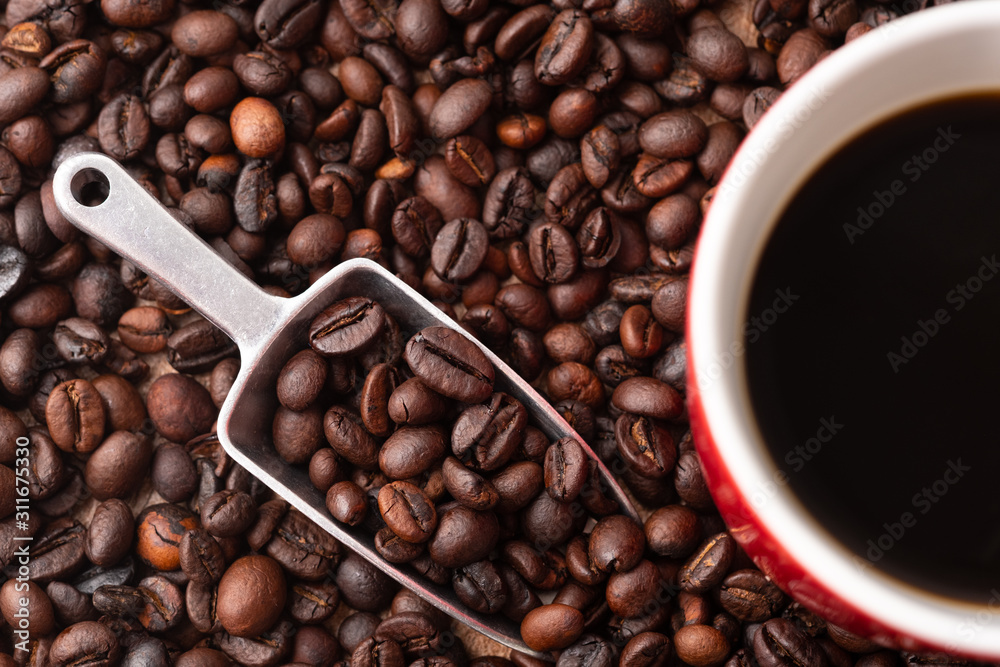 Fototapeta premium A cup of coffee, coffee beans and metal scoop. Red ceramic mug.