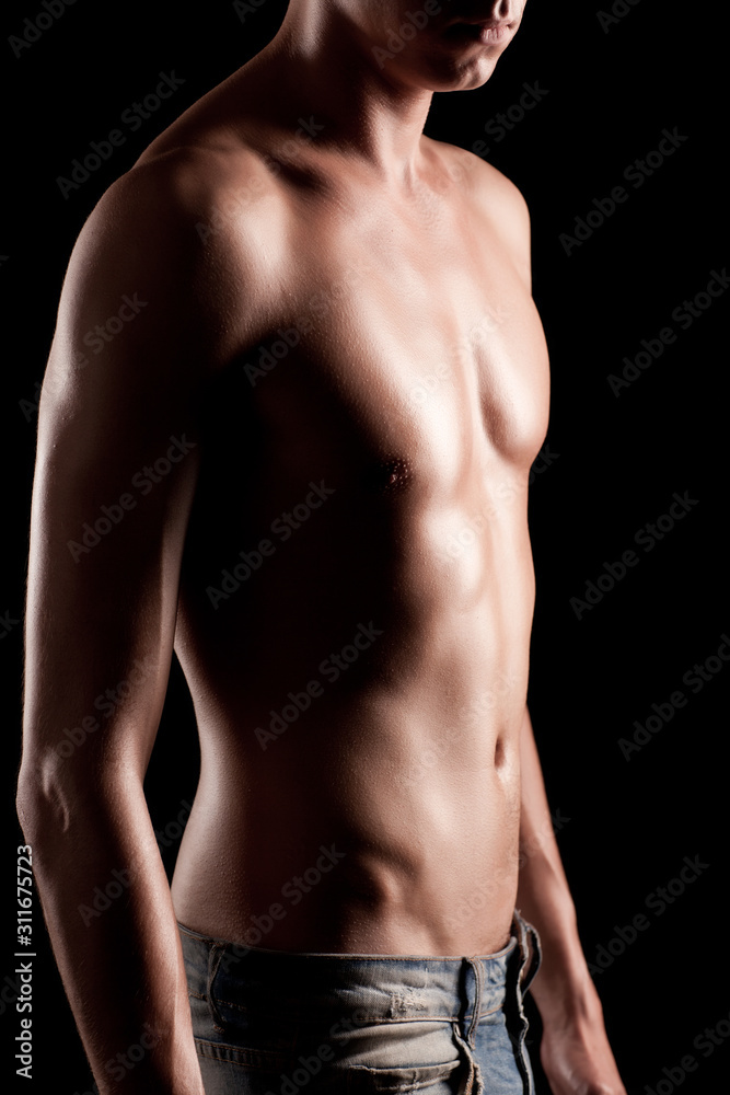 Young athletic man with naked torso in jeans standing over black background in photo studio. Beauty of man body and body relief concept Young athletic man with naked torso in jeans standing over black background in photo studio. Beauty of man body and body relief concept