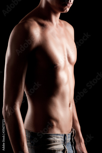 Young athletic man with naked torso in jeans standing over black background in photo studio. Beauty of man body and body relief concept