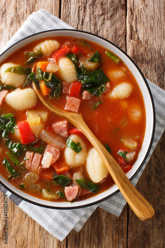 Tasty tomato soup with gnocchi, sausages and vegetables close-up in a bowl. Vertical top view