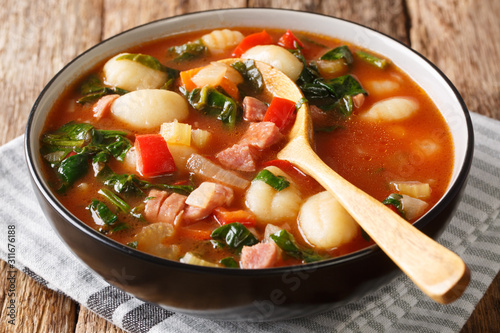 Traditional recipe for gnocchi soup with sausages,, tomato, spinach and vegetables close-up in a bowl. horizontal