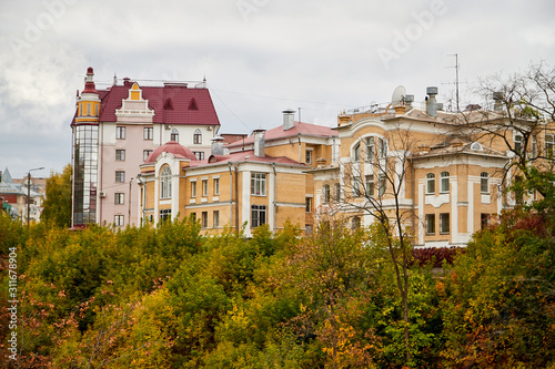 City houses with roofs and turrets and trees in the foreground on an autumn or summer day with clouds in the background