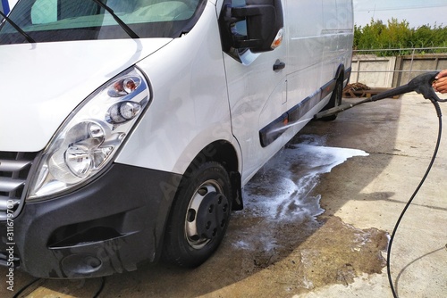 High pressure water jet cleaning. A male car wash's worker washing a white minibus using power sprayer.