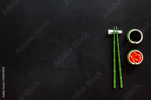 Set of chopsticks for sushi, ginger and soy sause on black background top-down frame copy space