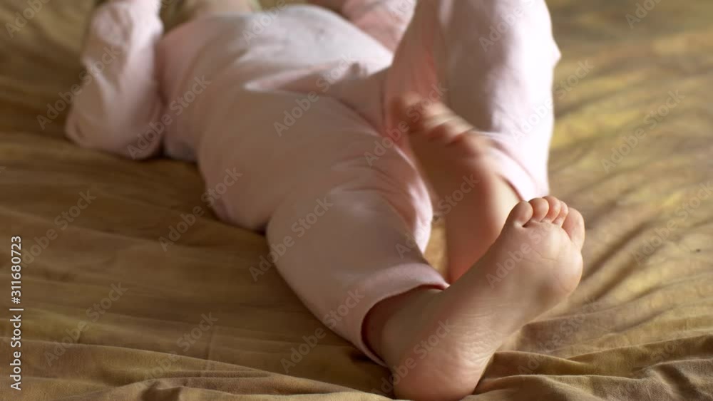 Legs, feet and fingers of boy close-up. Cute blond child in pink pajamas plays with touch screen of smartphone while lying on sofa. the kid wants learn everything. Home teaching for lagging children Stock Video | Adobe Stock