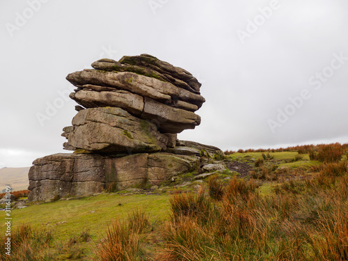 Wide angle view of a large granite tor rock formation among the moor grass on the cloudy hills of Dartmoor. Devon, United Kingdom. Travel and nature. photo