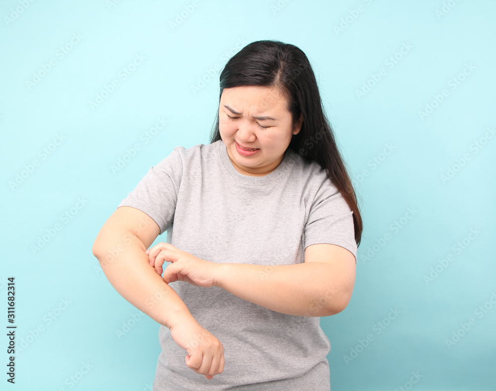Portrait Asia woman feel very itchy arm, on blue background in studio. Portrait Asia woman feel very itchy arm, on blue background in studio.