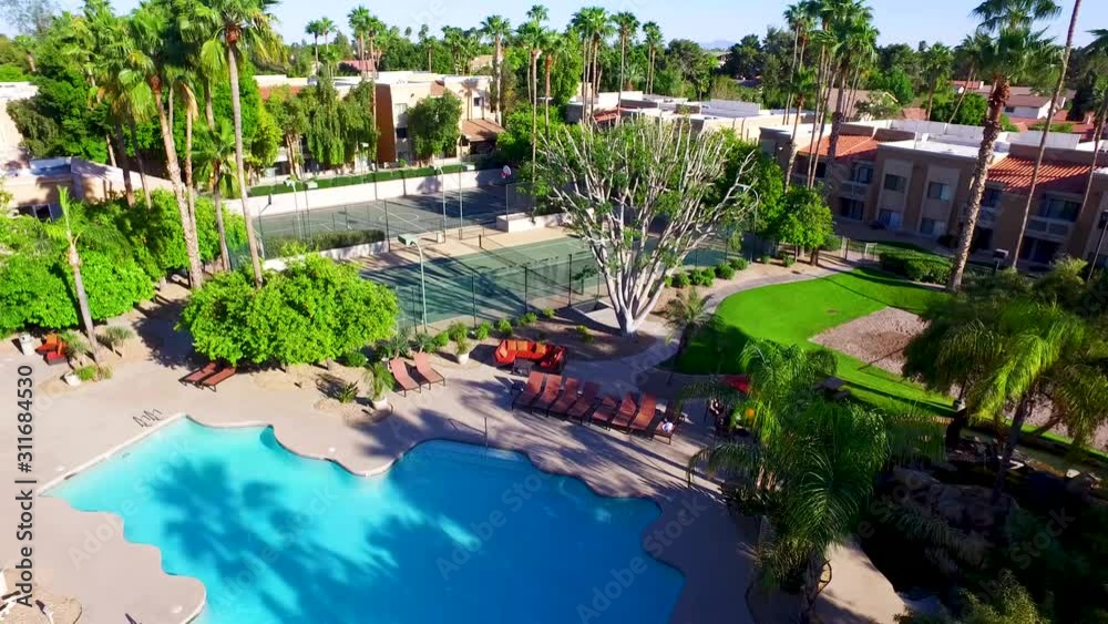 Aerial drone photography over a nice pool with palm trees and tennis courts. subtle camera movement gives the clip a cool look