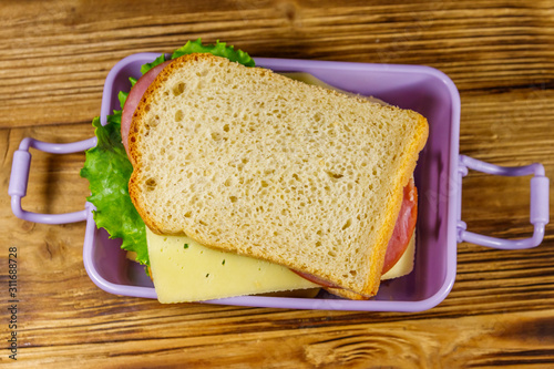 Lunch box with sandwiches on a wooden table. Top view