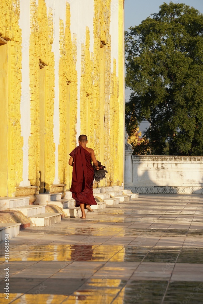 A novice monk holding an umbrella walking to the buddhist chapel