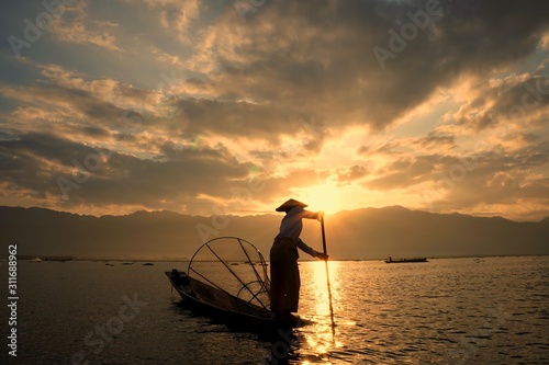 A fisherman with a coop sailing a boat on the Inle lake in the morning, Myanmar