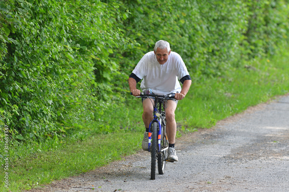 An older man is cycling on bike on a forest road in summer