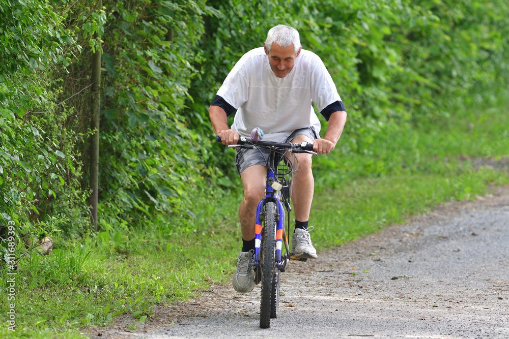 An older man is cycling on bike on a forest road in summer